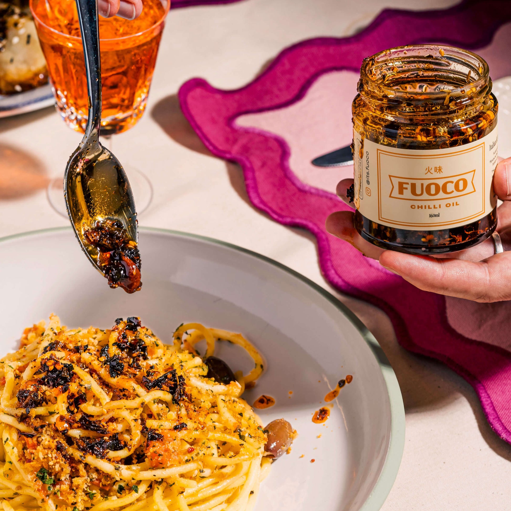 Fuoco crispy chilli oil 190ml hand holding jar pouring on noodles